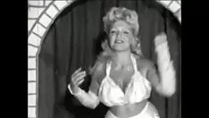 Oynat Brobdingnagian göğüsleri ile bukleli sarışın 60'ların seksi bir kamu sunumunda ayrı geçer